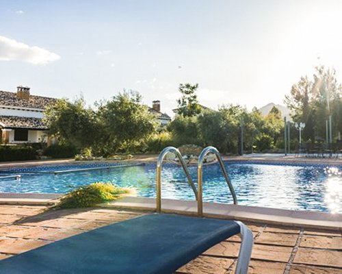 An outdoor pool with chaise lounge chairs alongside the resort and the trees.