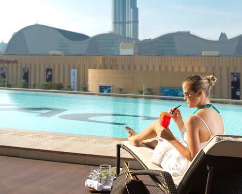 A woman having a cocktail alongside an outdoor swimming pool.