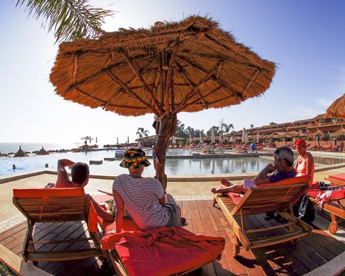 A view of the chaise lounge chairs and thatched sunshades alongside the swimming pool.