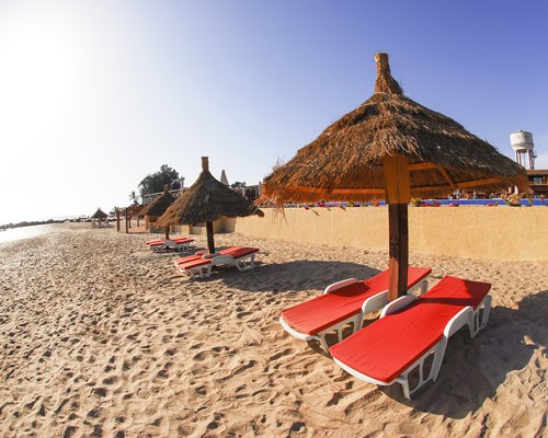 View of the beach with thatched sunshades and chaise lounge chairs.