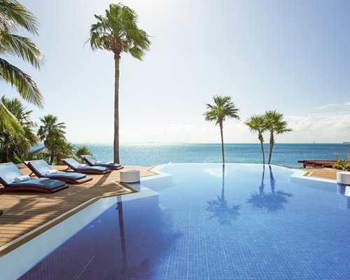 A large outdoor swimming pool with lounge chairs and trees alongside the beach.