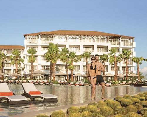 A couple in the outdoor swimming pool with in pool chaise lounge chairs alongside resort units.