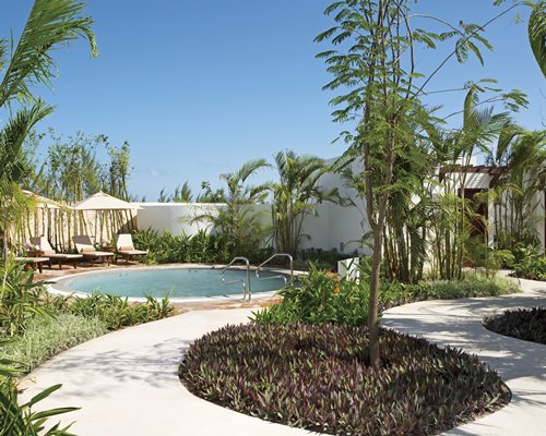 An outdoor hot tub with sunshades and chaise lounge chairs.