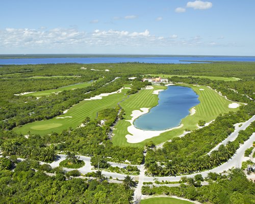 Aerial view of golf course and surrounded by wooded area alongside the sea.