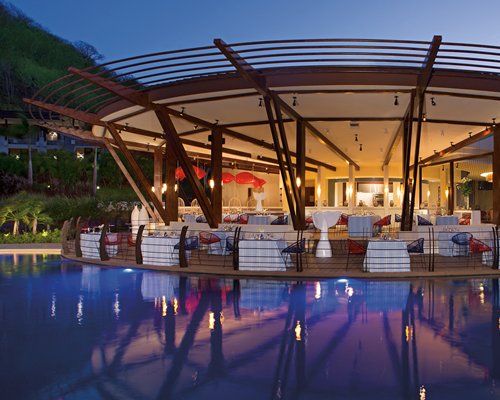 A well furnished fine dining area alongside the pool at dusk.