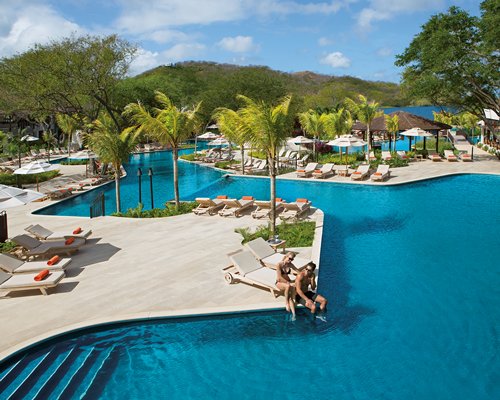 An outdoor swimming pool with chaise lounge chairs and sunshades.