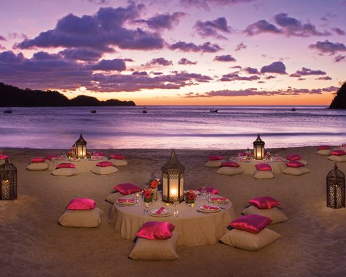 An outdoor dining area with lights alongside the beach at dusk.