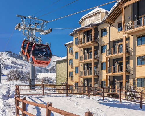 VIEW OF CABLE CARS ALONGSIDE MULTI STORY RESORT UNITS COVERED IN SNOW.