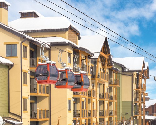 VIEW OF CABLE CARS ALONGSIDE MULTI STORY RESORT UNITS COVERED IN SNOW.