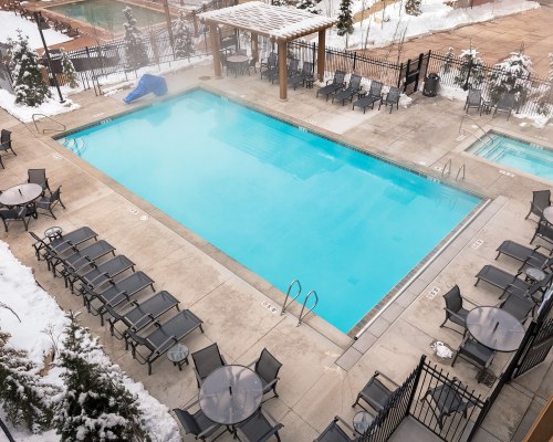AN OUTDOOR SWIMMING POOL AND HOT TUB WITH CHAISE LOUNGE CHAIRS AND PATIO FURNITURE COVERED IN SNOW.