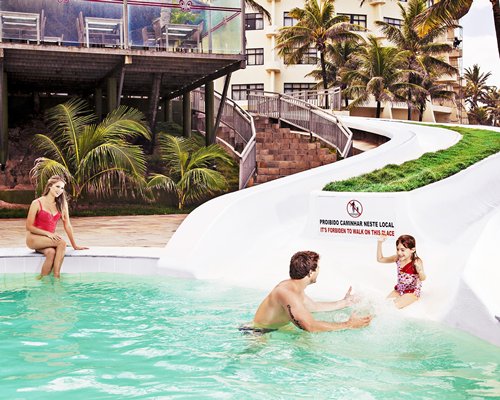 A family enjoying in an outdoor swimming pool with water slides alongside resort units.