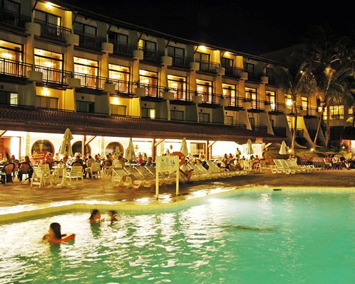 An outdoor swimming pool with chaise lounge chairs alongside the resort at night.