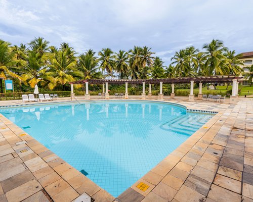 Outdoor swimming pool with chaise lounge chairs sunshades and palm trees alongside the unit.