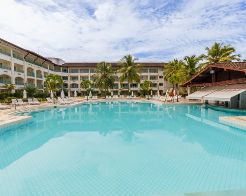Outdoor swimming pools with chaise lounge chairs and sunshades surrounded by palm trees.