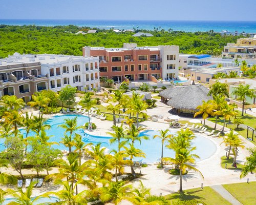 An outdoor swimming pool with chaise lounge chairs sunshades and trees alongside the resort units.