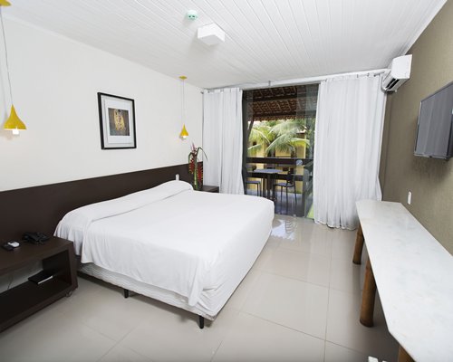 A well furnished bedroom with a queen bed television and balcony.