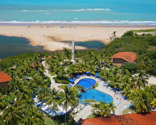 A balcony view of the swimming pool with chaise lounge chairs surrounded by trees alongside the beach.