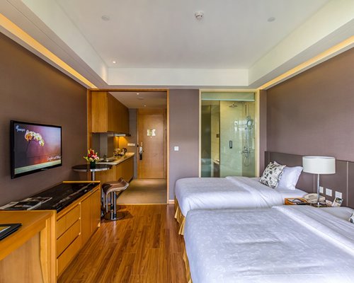 A well furnished bedroom with two queen beds television and a bathroom with shower stall.