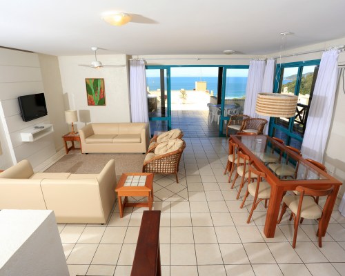 A WELL FURNISHED LIVING ROOM WITH A TELEVISION DINING AREA BALCONY AND OCEAN VIEW.
