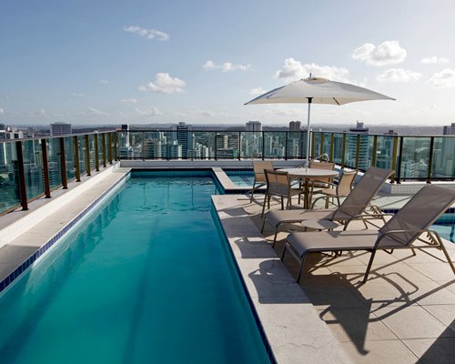 Outdoor swimming pool with chaise lounge chairs sunshade and view of skyscrapers.