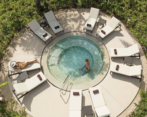An outdoor hot tub with chaise lounge chairs.