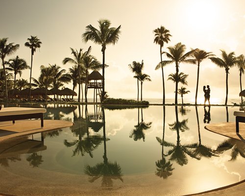 A couple enjoying the sunset by the outdoor pool and palm trees.