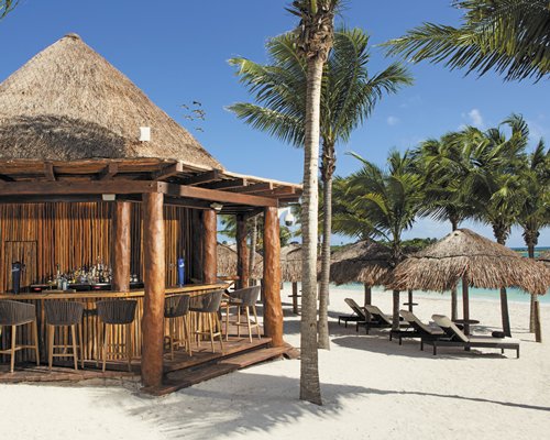 A view of the poolside bar with chaise lounge chairs and thatched sunshades alongside the sea.
