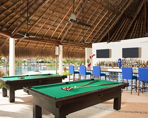 Covered bar with pool tables alongside an outdoor swimming pool.