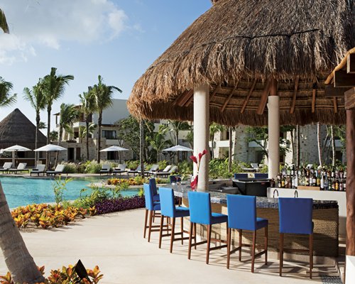 An outdoor swimming pools with chaise lounge chairs and sunshades alongside a poolside bar.