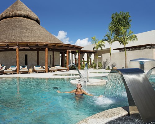 A woman relaxing in the outdoor swimming pool with the water curtains and chaise lounge chairs.