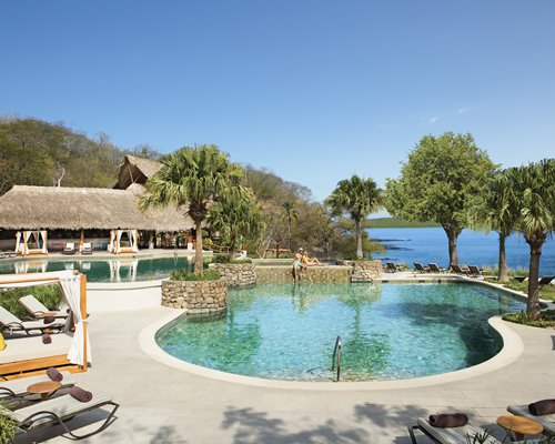 Outdoor swimming pools with chaise lounge chairs and beach beds alongside the ocean.
