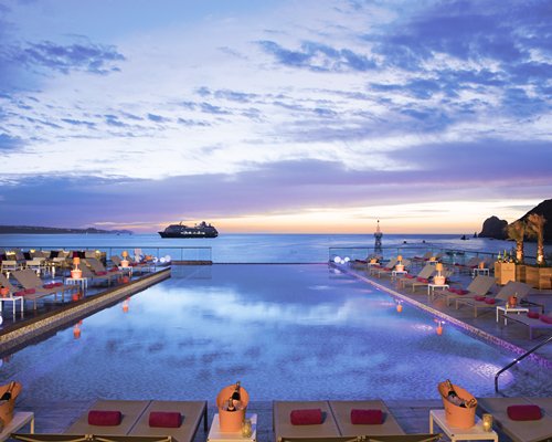 An outdoor swimming pool with chaise lounge chairs at dusk.