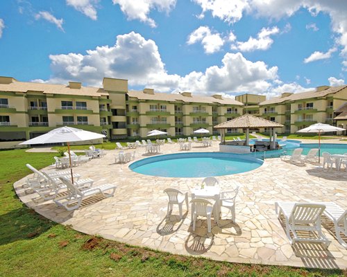 View of outdoor pools with chaise lounge chairs and sunshades alongside the multi story condo.