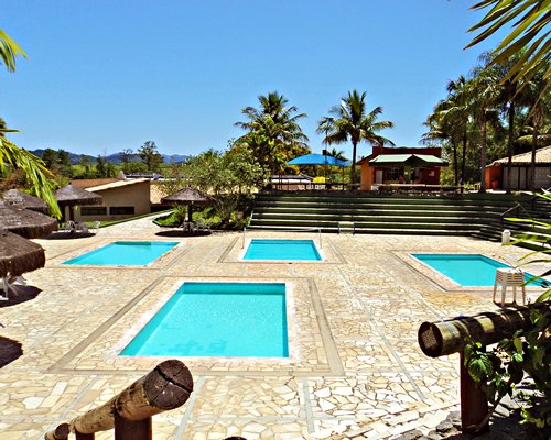 An outdoor kiddie pool with a patio and thatched sunshades.