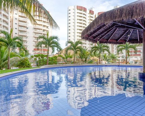 An outdoor swimming pool with thatches sunshade alongside multi story units.