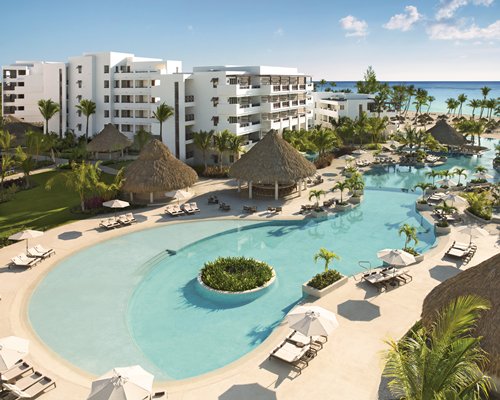 A large outdoor swimming pool with chaise lounge chairs and sunshades alongside multi story resort.