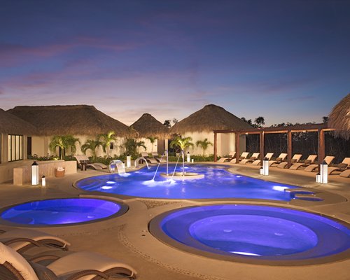 An outdoor swimming pool with hot tubs and chaise lounge chairs alongside resort units.
