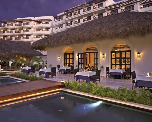 An outdoor fine dining restaurant alongside multi story resort units at dusk.