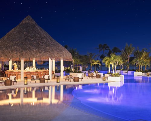 An outdoor swimming pool with trees and a poolside bar at night.