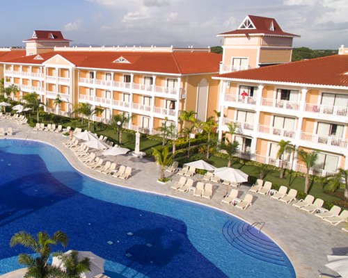 An outdoor swimming pool with chaise lounge chairs and sunshades alongside the resort.