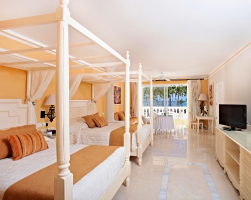 A WELL FURNISHED BEDROOM WITH TWO CANOPY BEDS AND A TELEVISION.