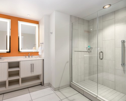 A BATHROOM WITH A STANDING SHOWER STALL AND DOUBLE SINK VANITY.