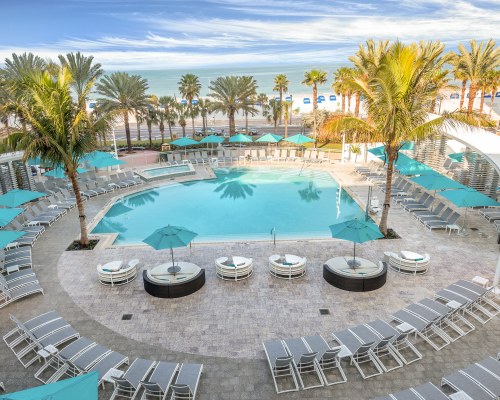 AN OUTDOOR SWIMMING POOL WITH CHAISE LOUNGE CHAIRS SUNSHADES AND GARDEN FURNITURE.