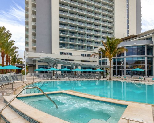 AN OUTDOOR SWIMMING POOL WITH HOT TUB CHAISE LOUNGE CHAIRS AND SUNSHADES ALONGSIDE THE RESORT UNIT.