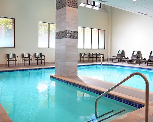 An indoor swimming pool with patio furniture and chaise lounge chairs.
