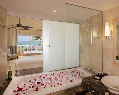 A bathtub shower and single sink vanity alongside well furnished bedroom with two beds.
