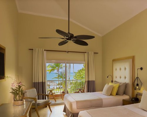 A well furnished bedroom with two beds and a balcony with patio furniture overlooking the beach.
