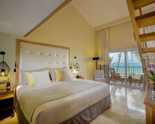 A well furnished bedroom and a balcony with patio furniture overlooking the beach.