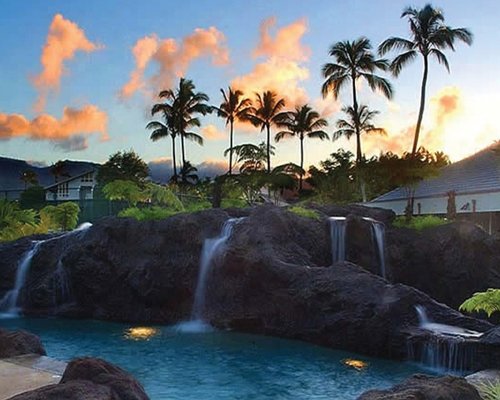 A view of resort pool with waterfalls and landscaped grounds at dusk.