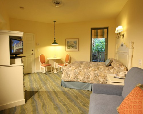 A WELL FURNISHED BEDROOM WITH LOVESEAT TELEVISION AND BALCONY WITH PATIO CHAIRS.
